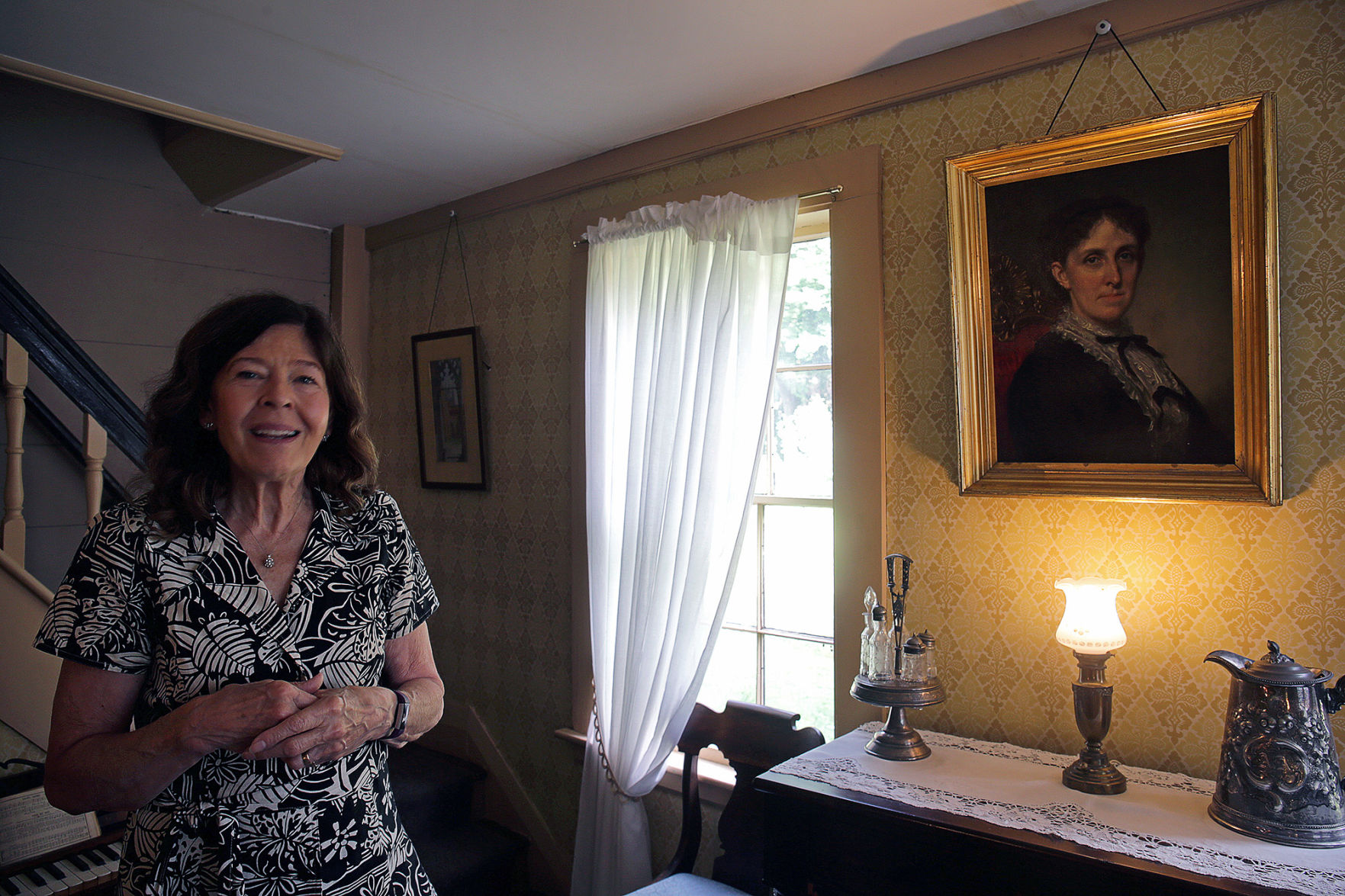 Jan Turnquist, executive director for Louisa May Alcott's Orchard House in Concord, Mass., poses next to a portrait of Louisa May Alcott done by George Healey, a famous portrait painter, on Sep. 11, 2018.